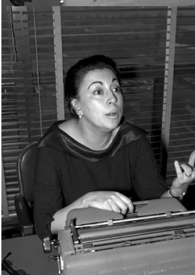Black-and-white photo of Rosario Castellanos sitting at a desk with a typewriter, gesturing as if mid-thought during the writing process.